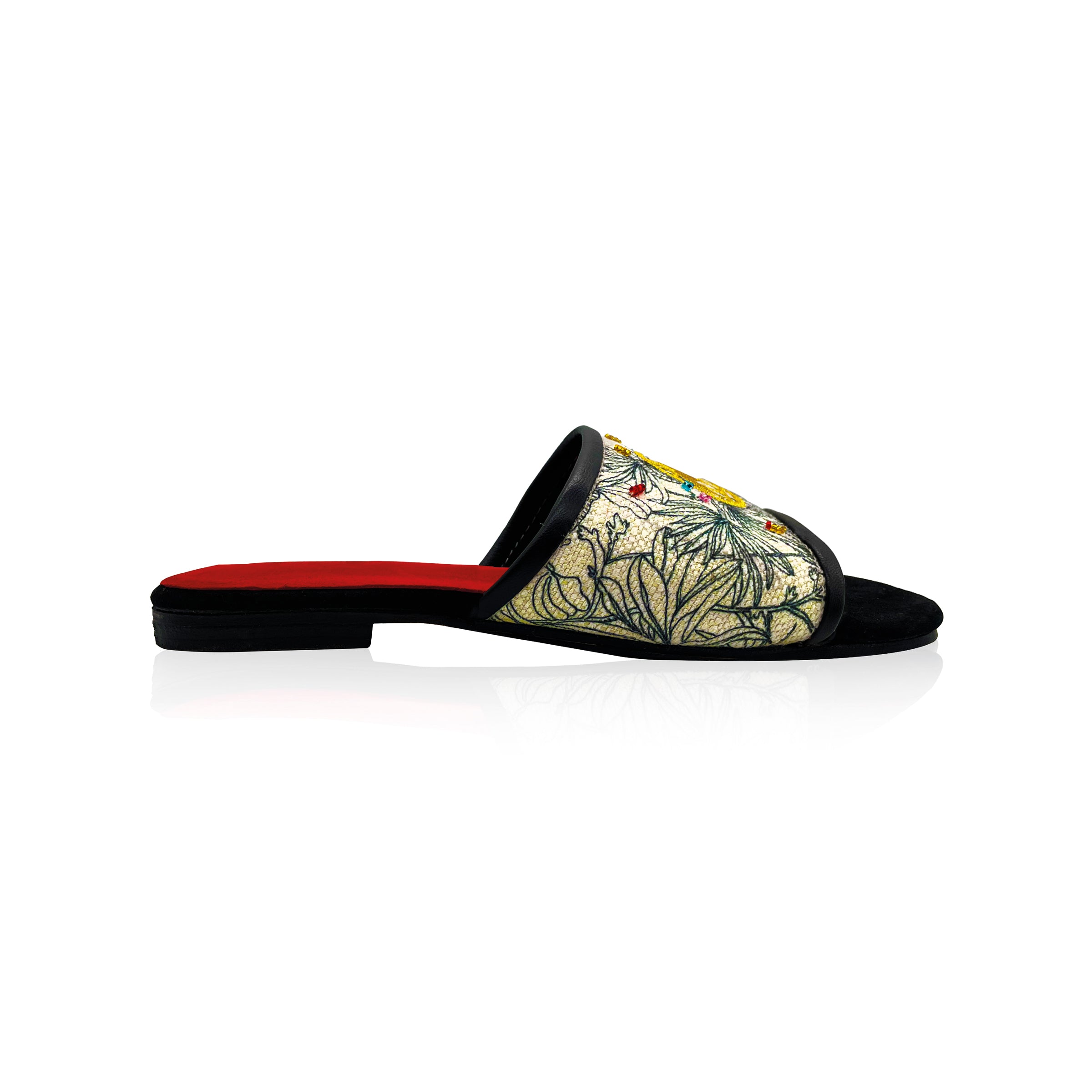 side view of black and white canvas slip on sandals with gold stitching and colored hand embroidered beads. Red leather interior and black leather toes
